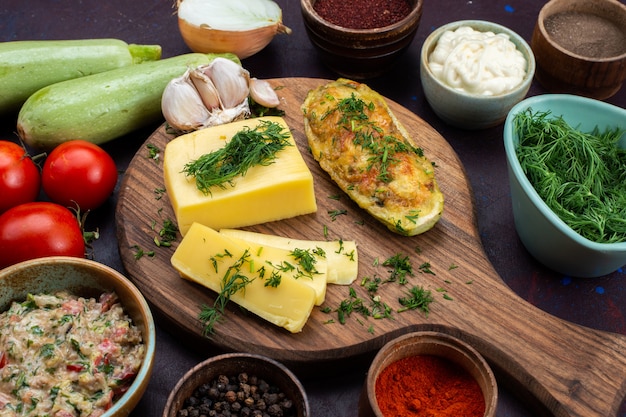 Gebackene Kürbisse aus der Nähe von oben mit grünem Käse, Gewürzen, Fleisch und frischem Gemüse auf einem dunklen Schreibtisch.