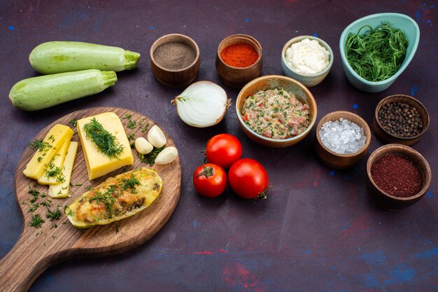 Gebackene Kürbisse mit halber Draufsicht mit Käse-Grün-Gewürzen, Hackfleisch und frischem Gemüse auf einem dunkelvioletten Schreibtisch.