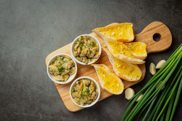 Gebackene Muschel mit Knoblauch und Butter, serviert mit Knoblauchbrot auf dunklem Hintergrund