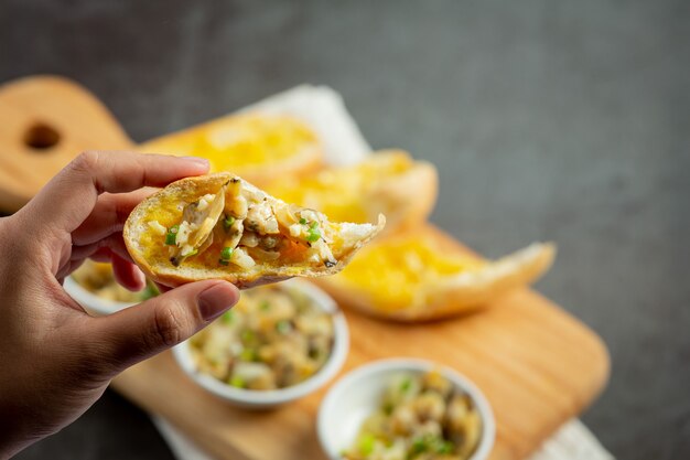 Gebackene Muschel mit Knoblauch und Butter, serviert mit Knoblauchbrot auf dunklem Hintergrund