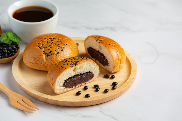 gebackene schwarze Bohnenpastenbrötchen auf Holzteller mit Kaffee serviert