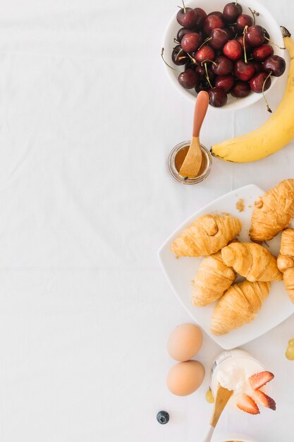 Gebackenes Croissant mit Früchten; Ei und Joghurt auf weißem Hintergrund
