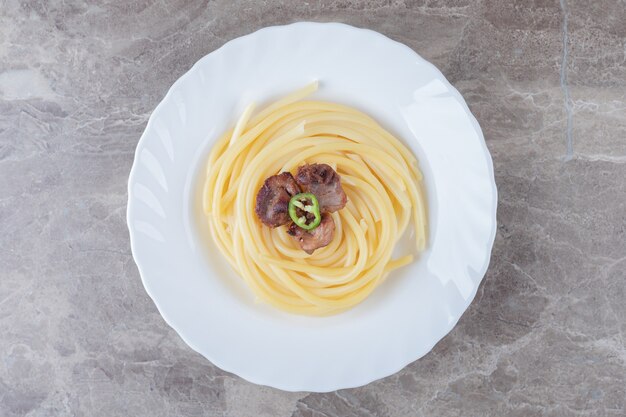 Gebackenes Fleisch über Nudeln auf dem Teller, auf der Marmoroberfläche.