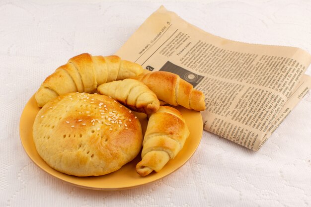 Gebäck und Croissants von oben in der orangefarbenen Platte zusammen mit Tapeten auf dem weißen Boden