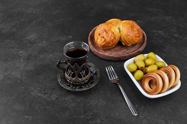 Gebäckbrötchen mit einem Glas Tee mit marinierten Oliven.