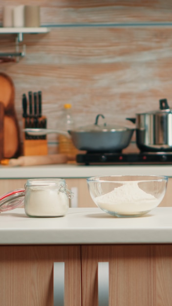 Gebäckzutaten für hausgemachte Kuchen und Brot in der leeren Küche. Modernes Esszimmer ausgestattet mit Kochutensilien mit Weizenmehl in Glasschüssel und frischen Eiern auf dem Tisch