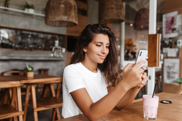 Gebräunte Frau im weißen T-Shirt schaut in Telefonbildschirm