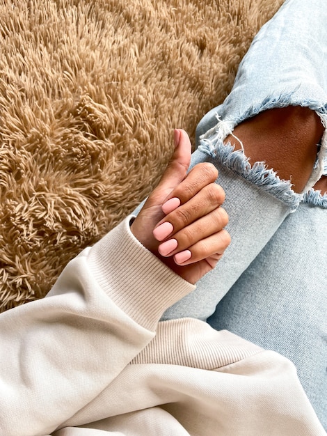 Gebräunte Hand einer Frau mit einer sanften beige-rosa Maniküre, die mit Gelpolitur bedeckt ist