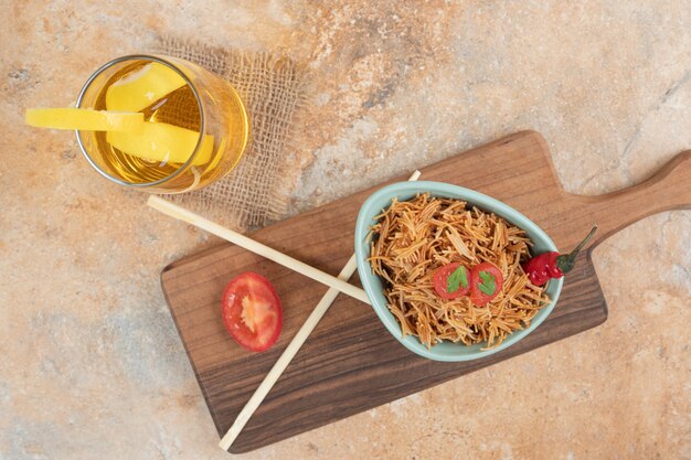 Gebratene Fadennudeln mit Tomate und Glas Saft auf Holzbrett