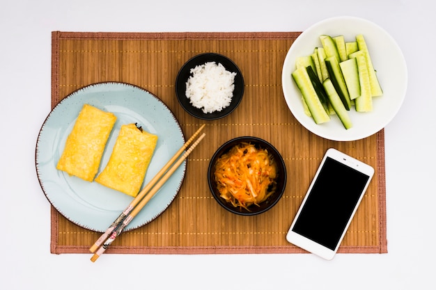 Gebratene Frühlingsrollen; Salat; gekochter Reis und geschnittene Zucchini mit Handy über Tischset