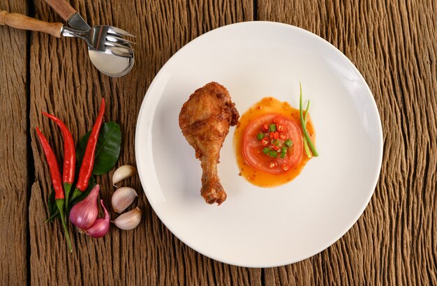 Gebratene Hähnchenschenkel auf einem weißen Teller mit Sauce und Knoblauch, Schalotte, Chili.
