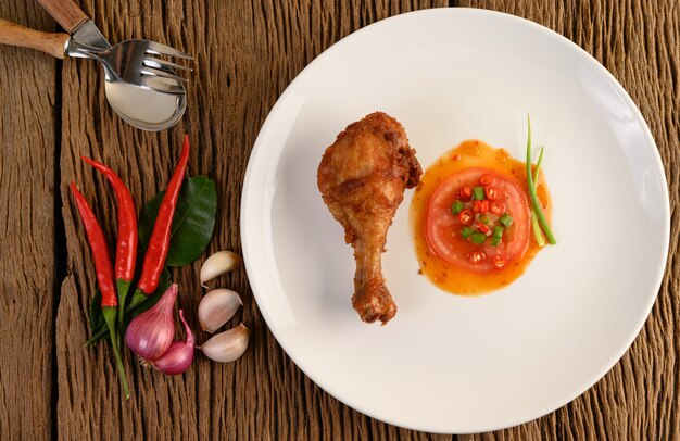 Gebratene Hähnchenschenkel auf einem weißen Teller mit Sauce und Knoblauch, Schalotte, Chili.