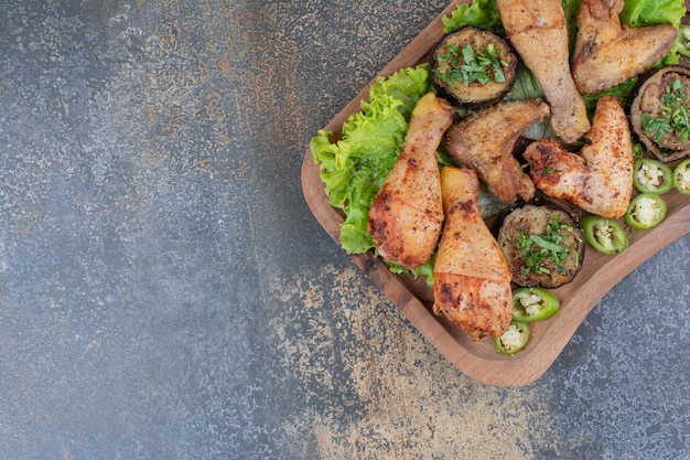Gebratene Hähnchenschenkel und Flügel auf Holzbrett mit Salat und Pfeffer. Foto in hoher Qualität