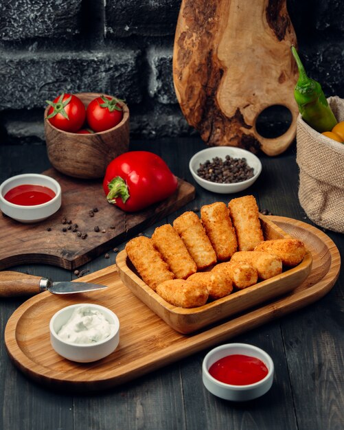 Gebratene Hähnchensticks auf einem Holzbrett mit Mayonnaise und Tomatensauce.