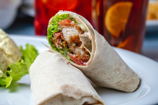 Gebratene Hähnchenstreifen von Seitenansicht mit Mayo-Tomate und Salat in Tortilla gewickelt