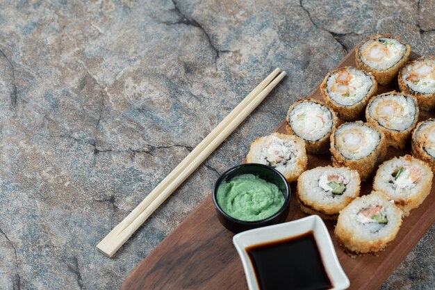 Gebratene heiße Sushi-Rollen mit Frischkäse, Wasabi und Sojasauce auf einem Holzbrett.