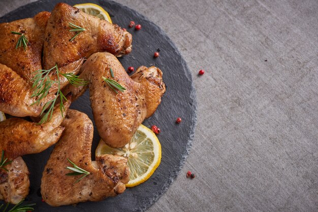 Gebratene Hühnerflügel in Barbecue-Sauce mit Pfeffersamen Rosmarin, Salz in einer schwarzen Steinplatte auf einem grauen Steintisch.