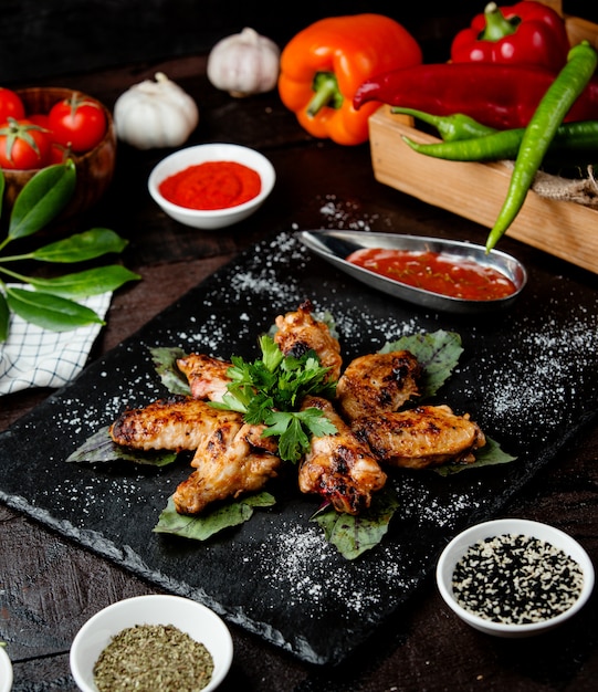 Gebratene Hühnerflügel mit Sauce in schwarzen Gerichten