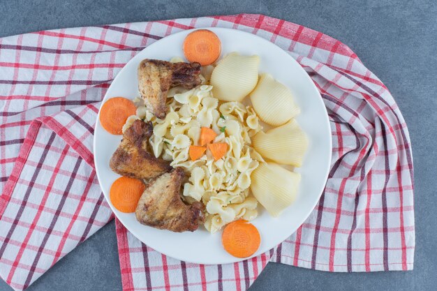 Gebratene Hühnerflügel und Nudeln auf weißem Teller.