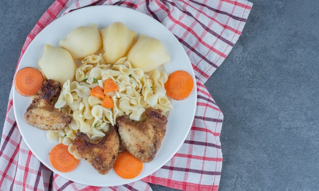 Gebratene Hühnerflügel und Nudeln auf weißem Teller.