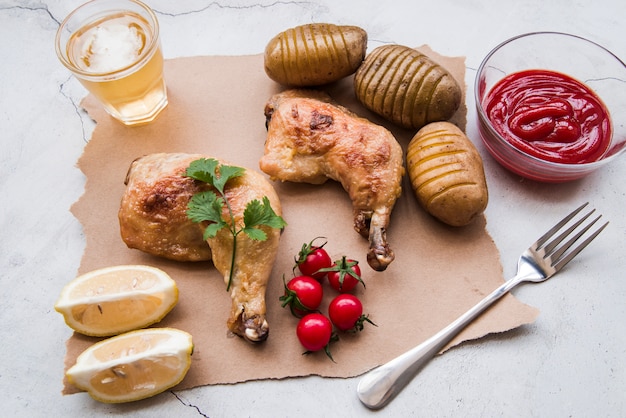 Kostenloses Foto gebratene hühnerkeule; gekochte kartoffel; soße; kirschtomate; zitrone; gabel und bier zum abendessen auf verwittertem hintergrund