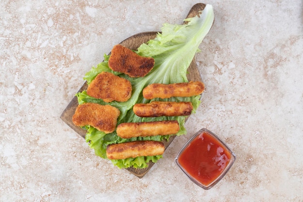 Gebratene Hühnernuggets und gegrillte Würstchensticks auf einem Stück Salat serviert mit Ketchup.