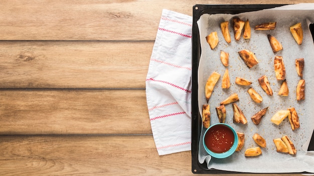 Gebratene Kartoffelstücke mit Ketschup im Behälter über Holztisch