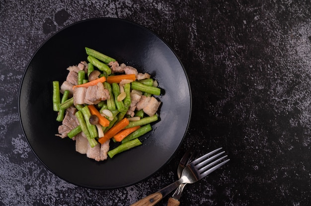Gebratene lange Bohnen und Karotten, Schweinebauch hinzufügen, auf einen schwarzen Teller legen.
