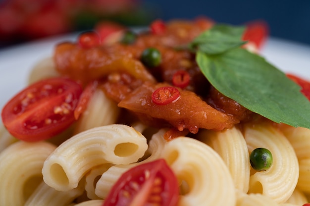 Gebratene Makkaroni mit Tomaten, Chili, Pfeffersamen und Basilikum in einer weißen Schale.