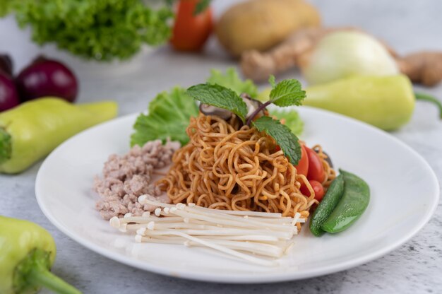 Gebratene Nudeln mit gehacktem Schweinefleisch, Edamame, Tomaten und Pilzen auf einem weißen Teller.