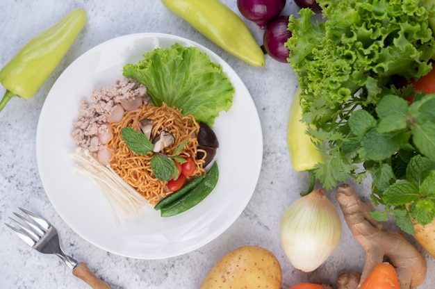 Gebratene Nudeln mit gehacktem Schweinefleisch, Edamame, Tomaten und Pilzen auf einem weißen Teller.