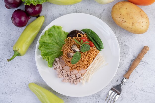 Gebratene Nudeln mit gehacktem Schweinefleisch, Edamame, Tomaten und Pilzen auf einem weißen Teller.