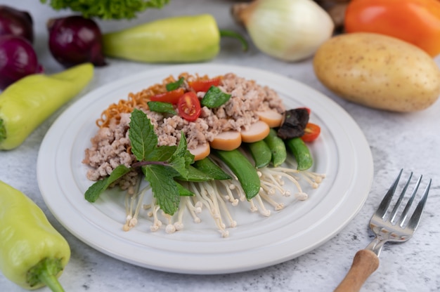 Gebratene Nudeln mit gehacktem Schweinefleisch, Edamame, Tomaten und Pilzen auf einem weißen Teller.