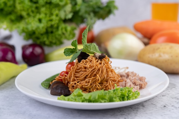 Gebratene Nudeln mit gehacktem Schweinefleisch, Edamame, Tomaten und Pilzen auf einem weißen Teller.