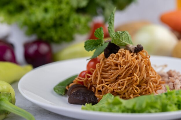 Gebratene Nudeln mit gehacktem Schweinefleisch, Edamame, Tomaten und Pilzen auf einem weißen Teller.