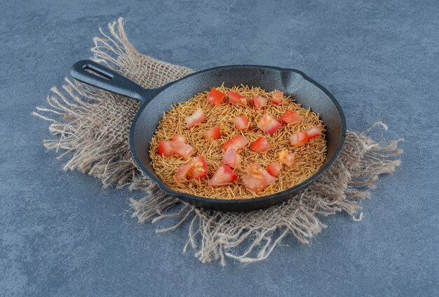 Gebratene Nudeln mit Tomatenscheiben auf schwarzer Pfanne.