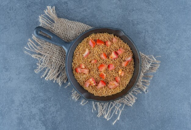 Gebratene Nudeln mit Tomatenscheiben auf schwarzer Pfanne.