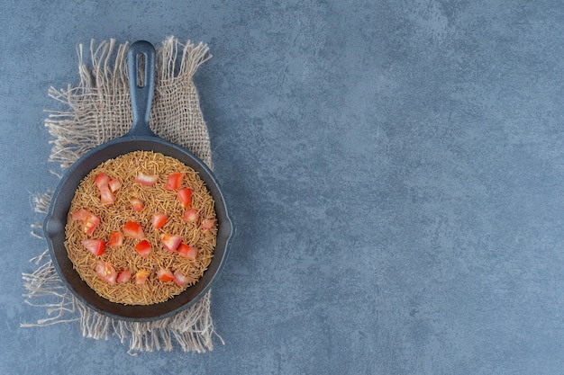 Gebratene Nudeln mit Tomatenscheiben auf schwarzer Pfanne.