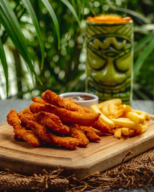 Gebratene panierte Hähnchenbruststreifen mit Ketchup und Pommes Frites auf einem Holzbrett