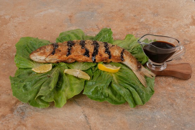 Gebratener Fisch auf Salat mit Zitronenscheiben, Gurken und Granatapfelsauce.