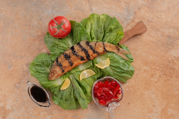 Kostenloses Foto gebratener fisch auf salat mit zitronenscheiben, gurken und granatapfelsauce.