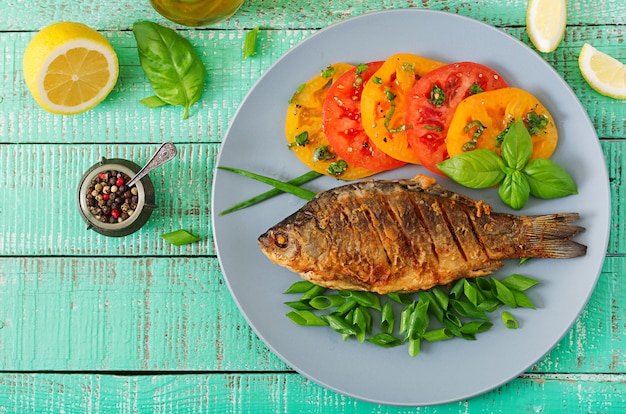 Gebratener Fischkarpfen und frischer Gemüsesalat auf Holztisch. Flach liegen. Draufsicht