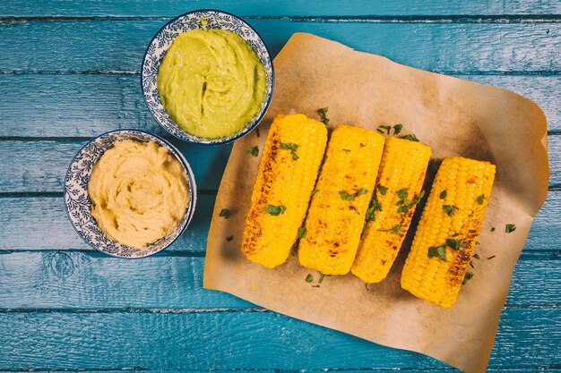 Gebratener organischer Zuckermais mit Guacamole und Soße auf blauem Holztisch