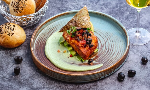 Gebratenes Fischfilet auf Avocado-Scheiben und Sauce mit Tomatenolive und Fischschale