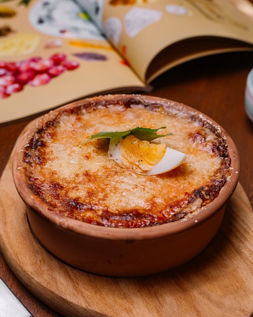 Gebratenes italienisches Gericht in einer mit geschmolzenem Käse und gekochter Eihälfte garnierten Keramikpfanne
