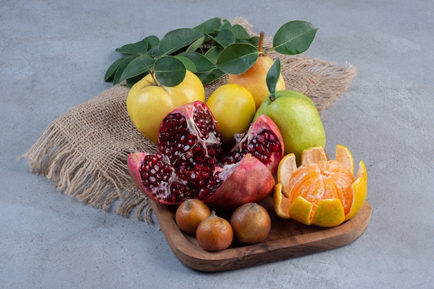 Gebrochener Granatapfel, geschälte Mandarine und ganze Quitten und Birnen auf einem Stück Stoff auf Marmorhintergrund.