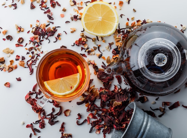 Gebrühter Tee mit getrockneten Kräutern, Zitrone im Glas und Teekanne auf weißer Oberfläche