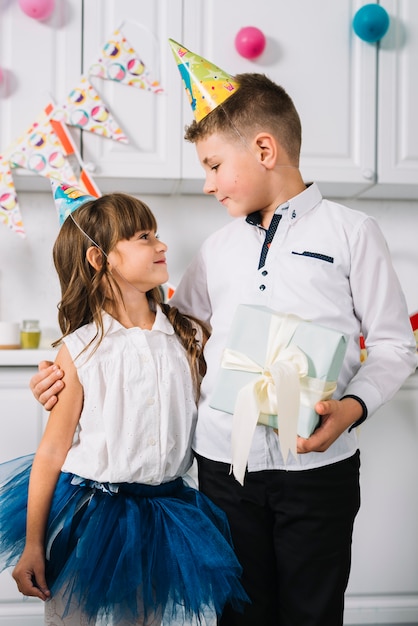 Kostenloses Foto geburtstagsjunge, der die geschenkbox in der hand steht mit ihrer schwester einander betrachtend hält