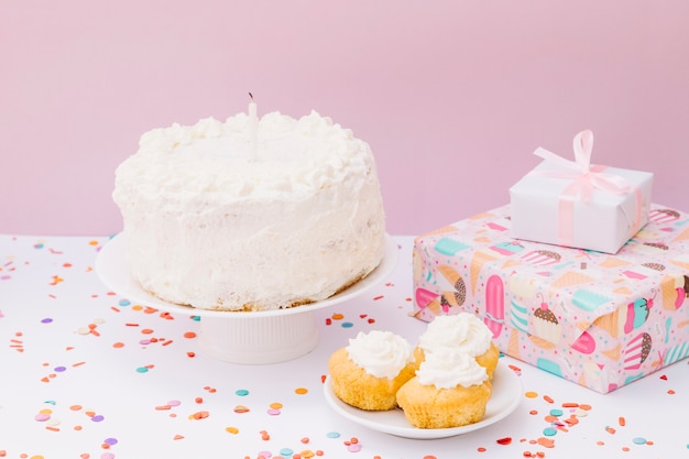 Kostenloses Foto geburtstagskuchen; muffins und geschenkboxen mit konfetti auf weißem schreibtisch vor rosa hintergrund