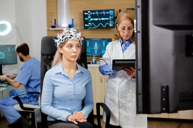 Geduldige Frau mit Scangerät auf dem Kopf und Arzt, der es mit Tablet in der Hand plant. Neurologische Klinik